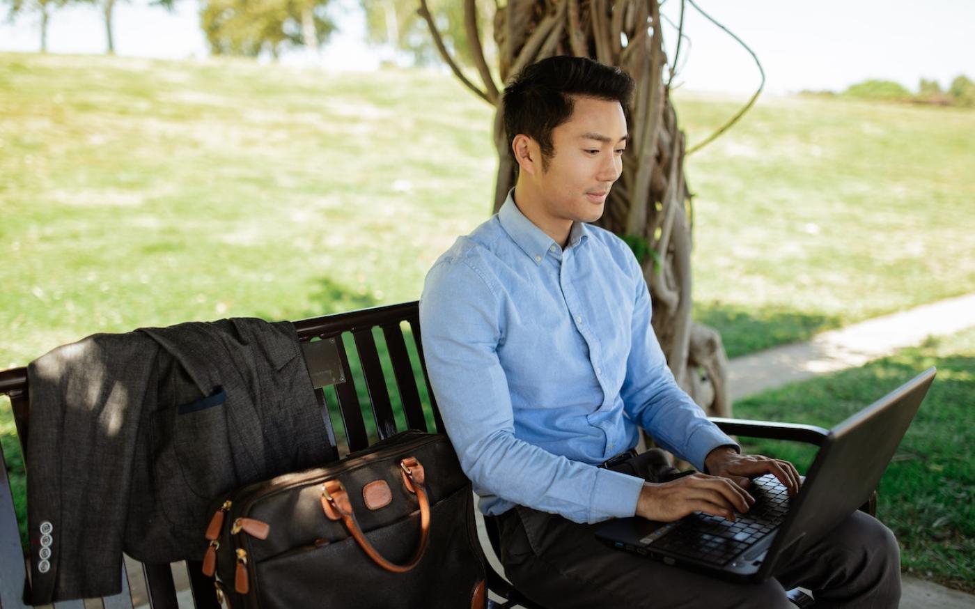 Man sitting on a park bench and working on a laptop