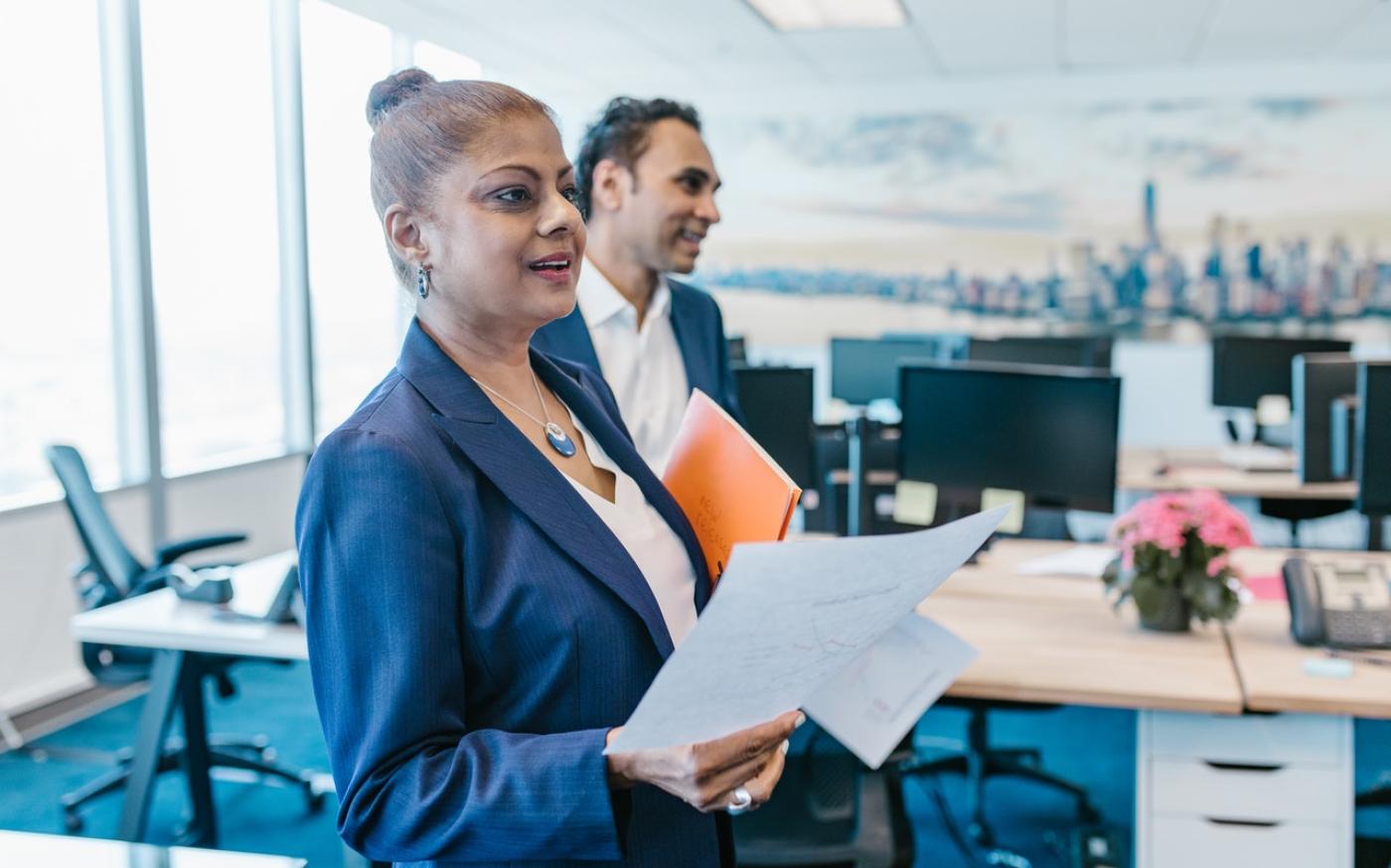 Woman in a suit holding a piece of paper. She is in an office setting.